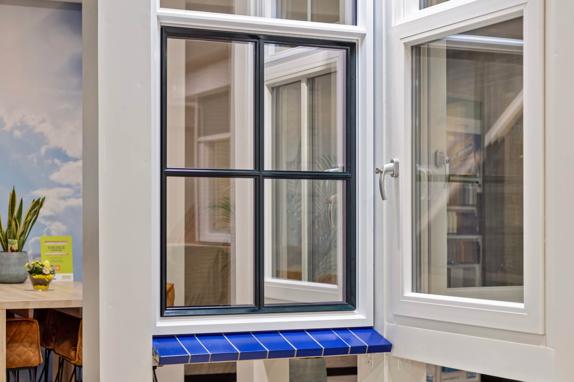 Wit kunststof draaikiepraam met zwarte roedes en blauwe vensterbank in de showroom van Bendabouw