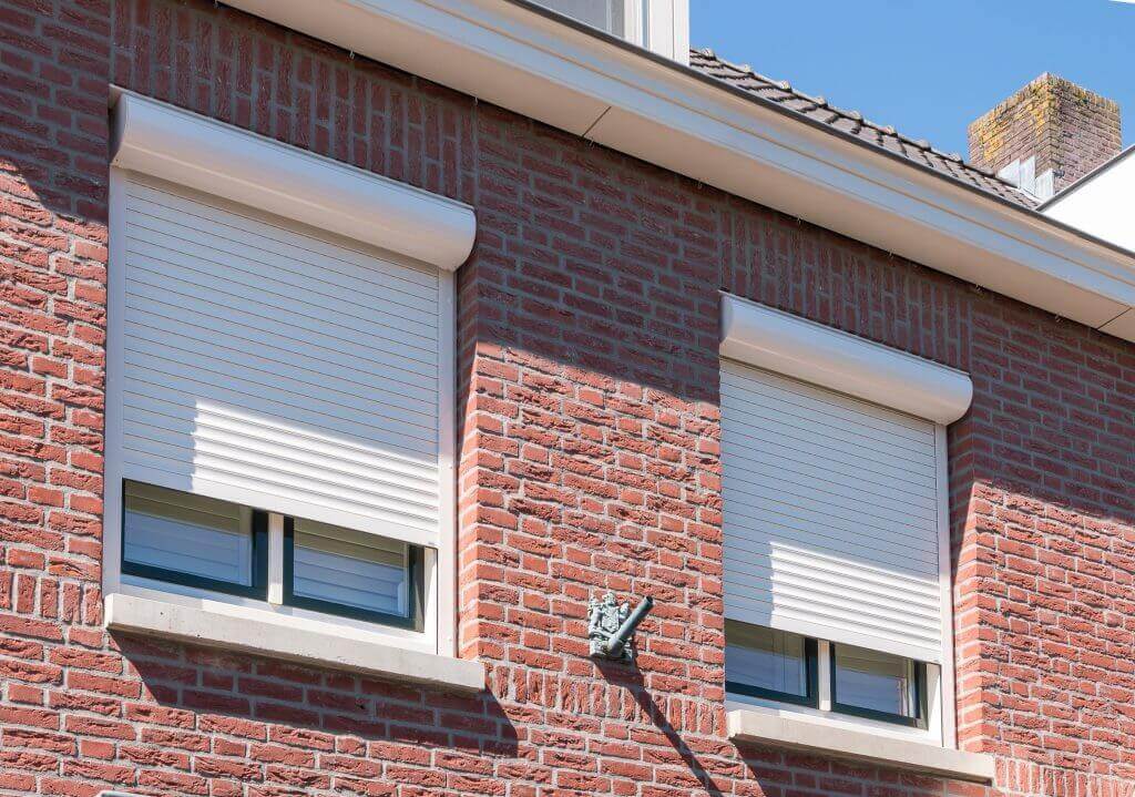 Witte rolluiken met kast boven de ramen van een woning met rode bakstenen gevel